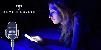 A young woman lying in bed at night, illuminated by the blue light of her phone screen