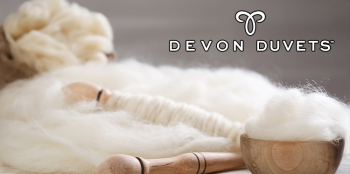 Soft raw wool with wooden spinning tools, featuring the Devon Duvets logo in the corner.