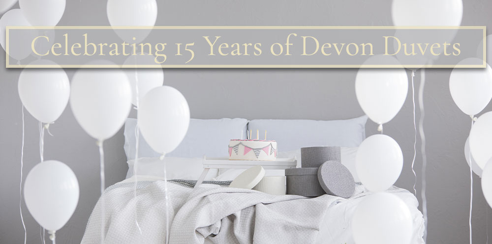 Celebrating 15 years of Devon Duvets with a cake on a bed with balloons