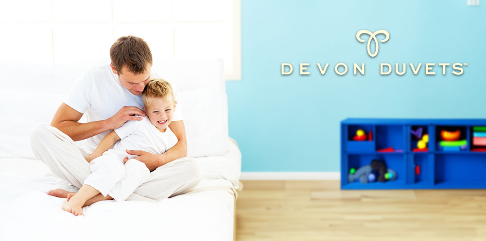 A lifestyle shot of a child and his father playing in the bedroom with Devon Duvets.