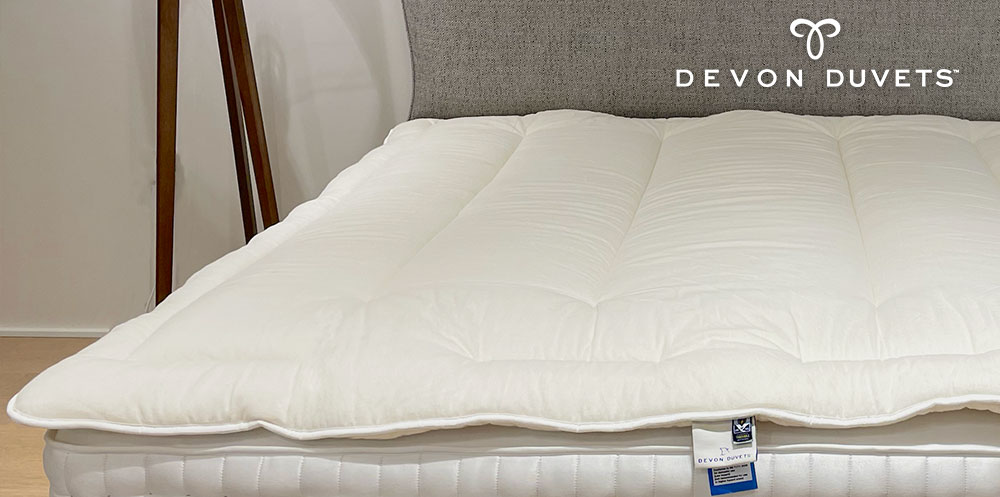 A beautifully crafted Devon Duvets mattress topper showcased on a bed, ready to offer the perfect balance of comfort and temperature regulation for a restful night's sleep.