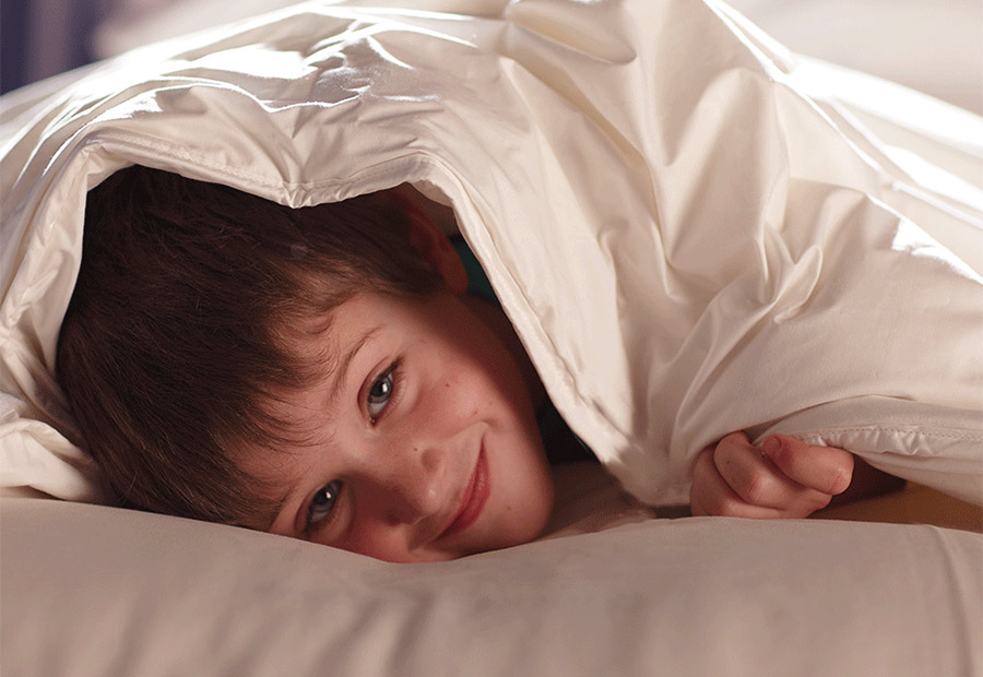 Child resting beneath a lightweight breathable wool duvet in a calm bedroom.