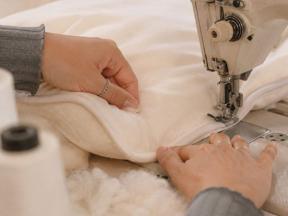 A maker finishing the stitching on a piece of bedding.