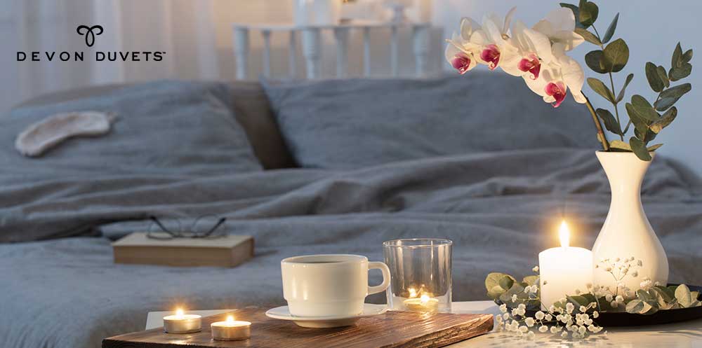 A romantic candlelit dinner setting in front of a luxuriously handcrafted Devon Duvets wool bedding, symbolising the warmth and comfort our products bring to your personal spaces.