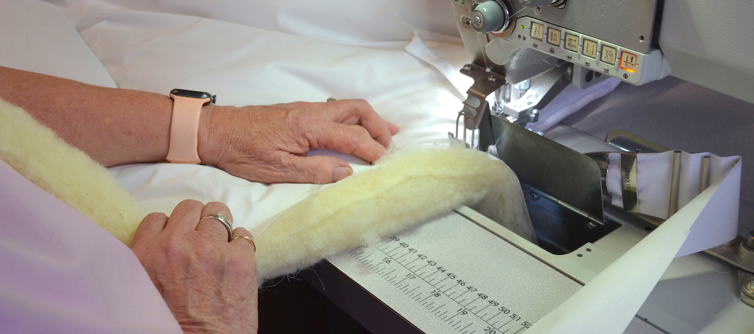 A close up shot of a hand sewing a wool duvet and using a dewing machine.