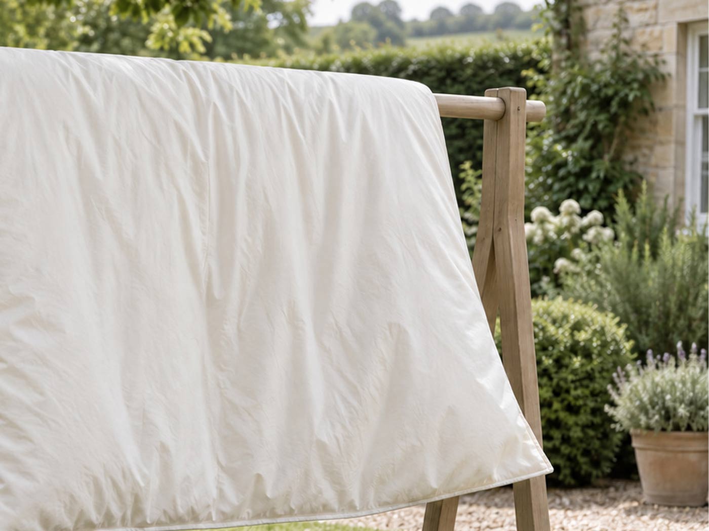 A cream duvet airing over a broad outdoor rail in a shaded garden