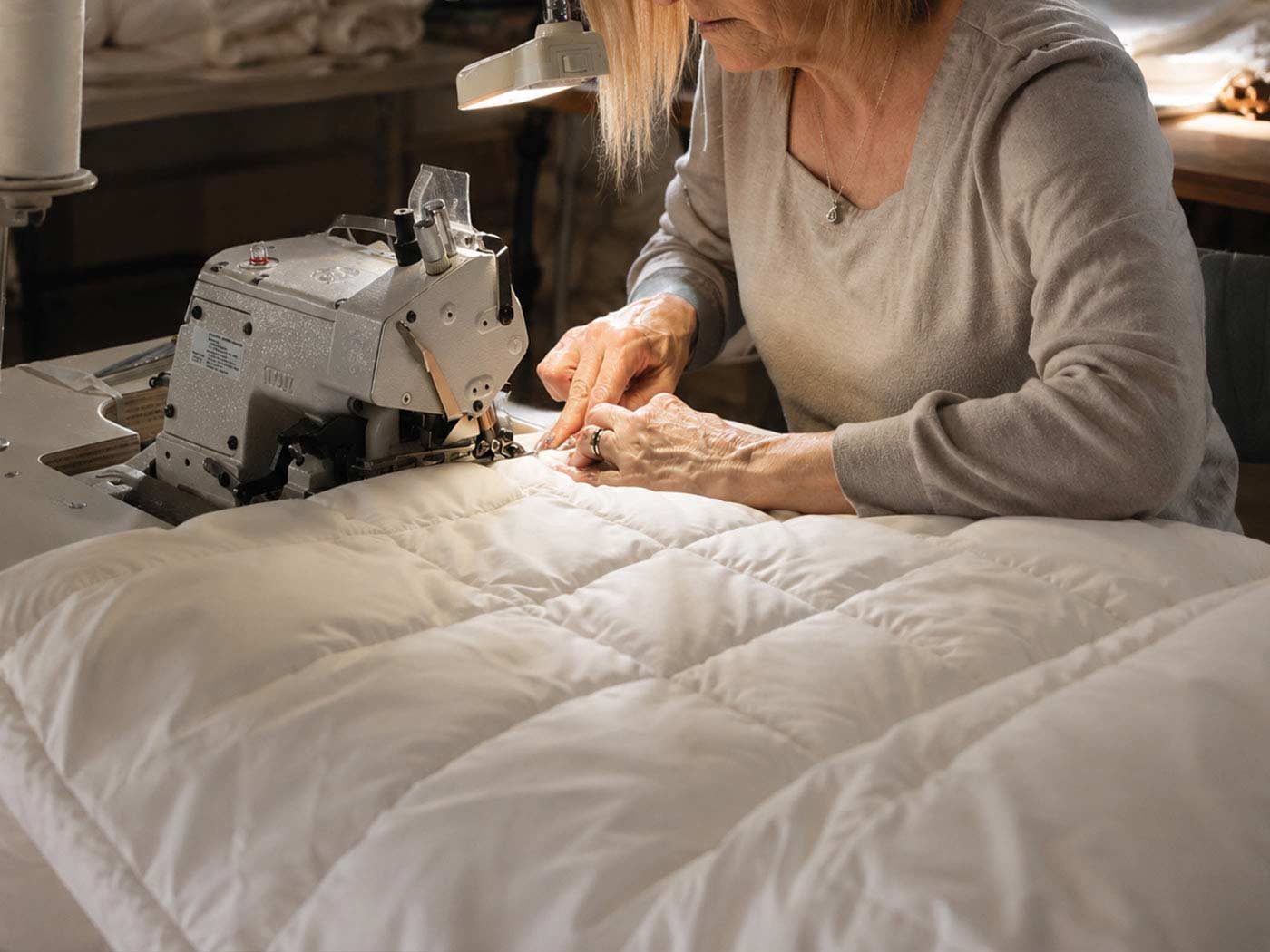 A maker checking and finishing the edge of a wool mattress topper by hand