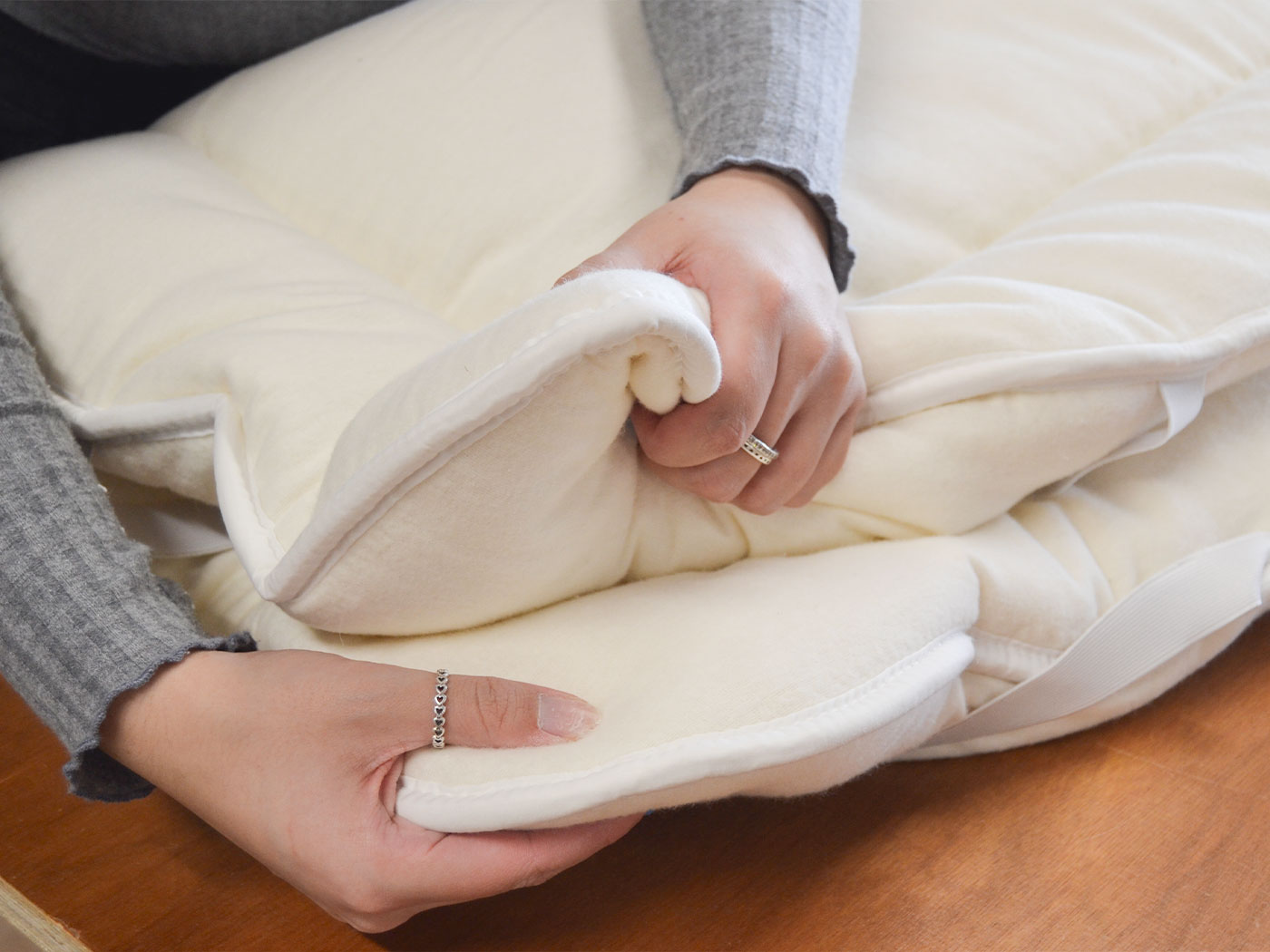 A maker gently checking the soft edge and flexible feel of a cotton-covered wool mattress topper