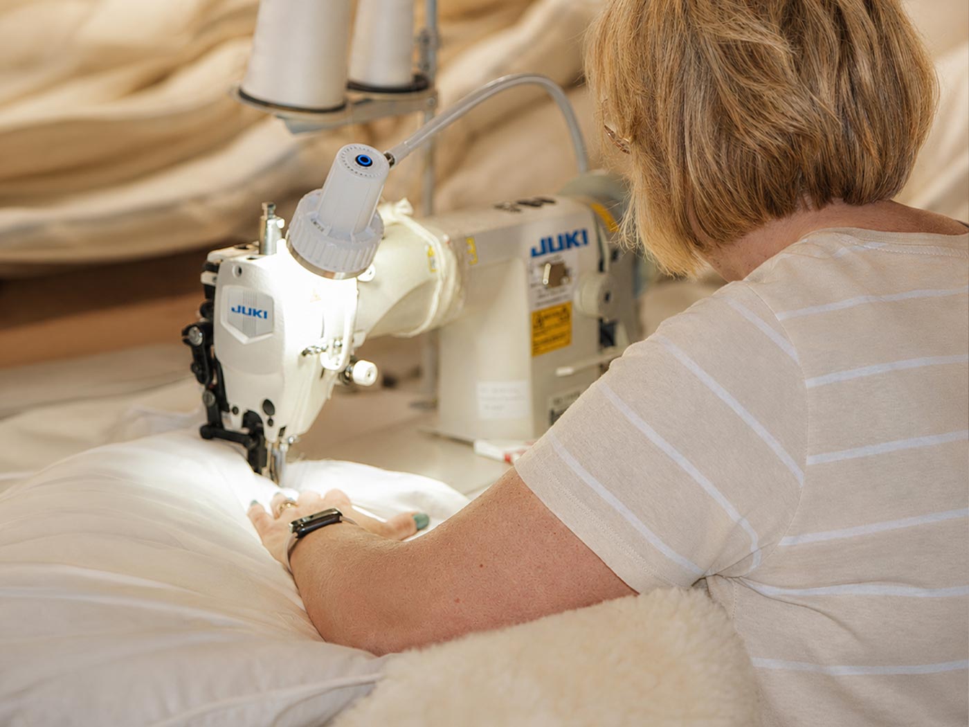 Skilled hands guiding the cotton edge of wool bedding beneath a sewing machine needle