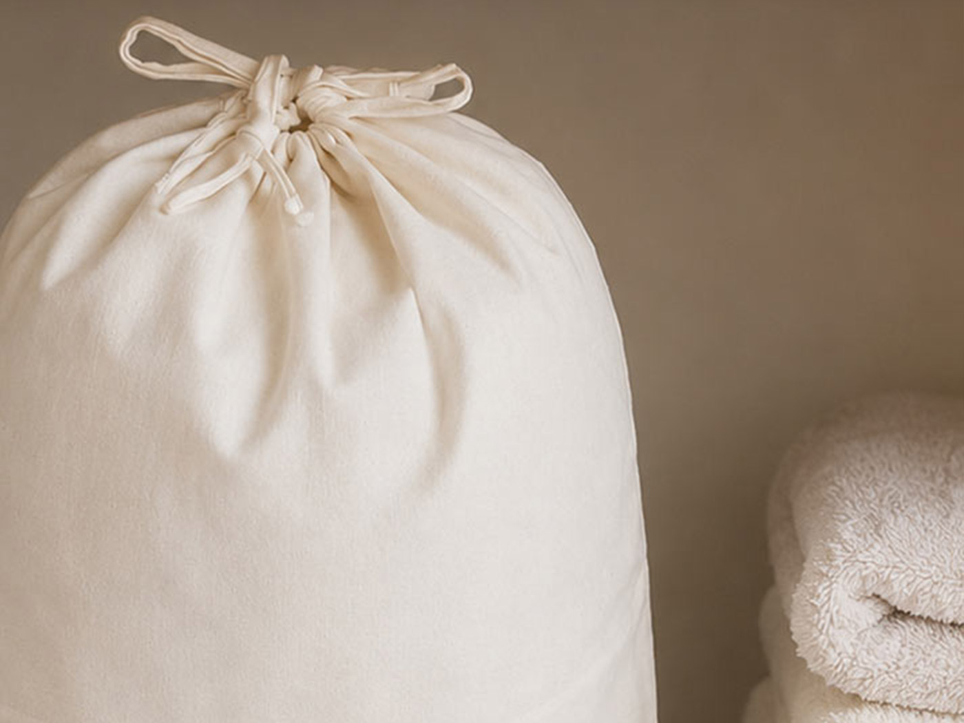A folded cream duvet inside an open breathable cotton storage bag