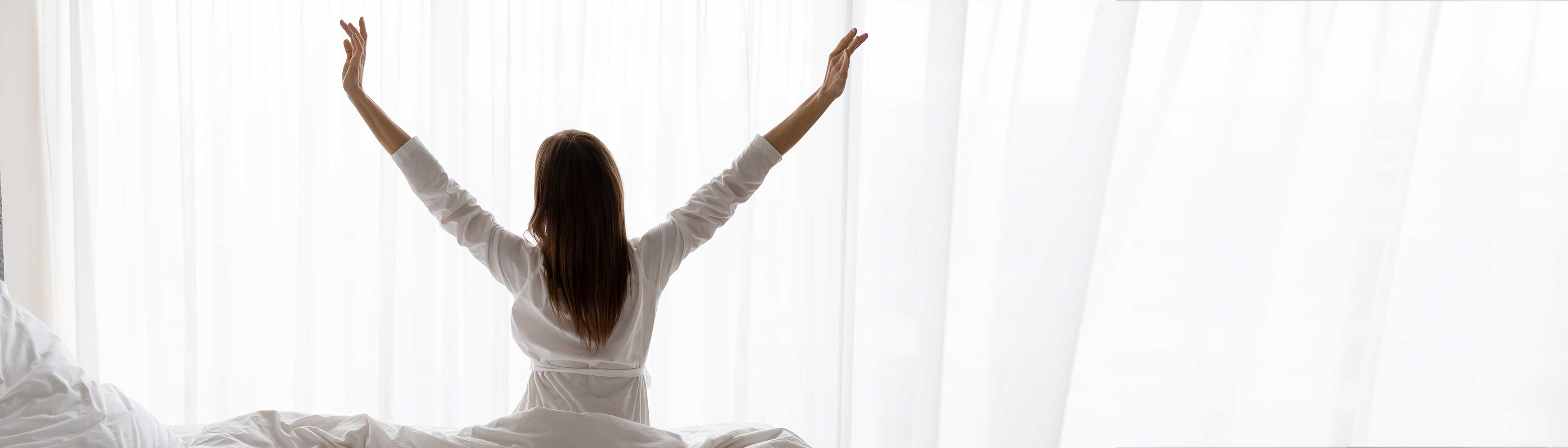 Happy woman waking up refreshed after a good night's sleep with Devon Duvets on World Sleep Day